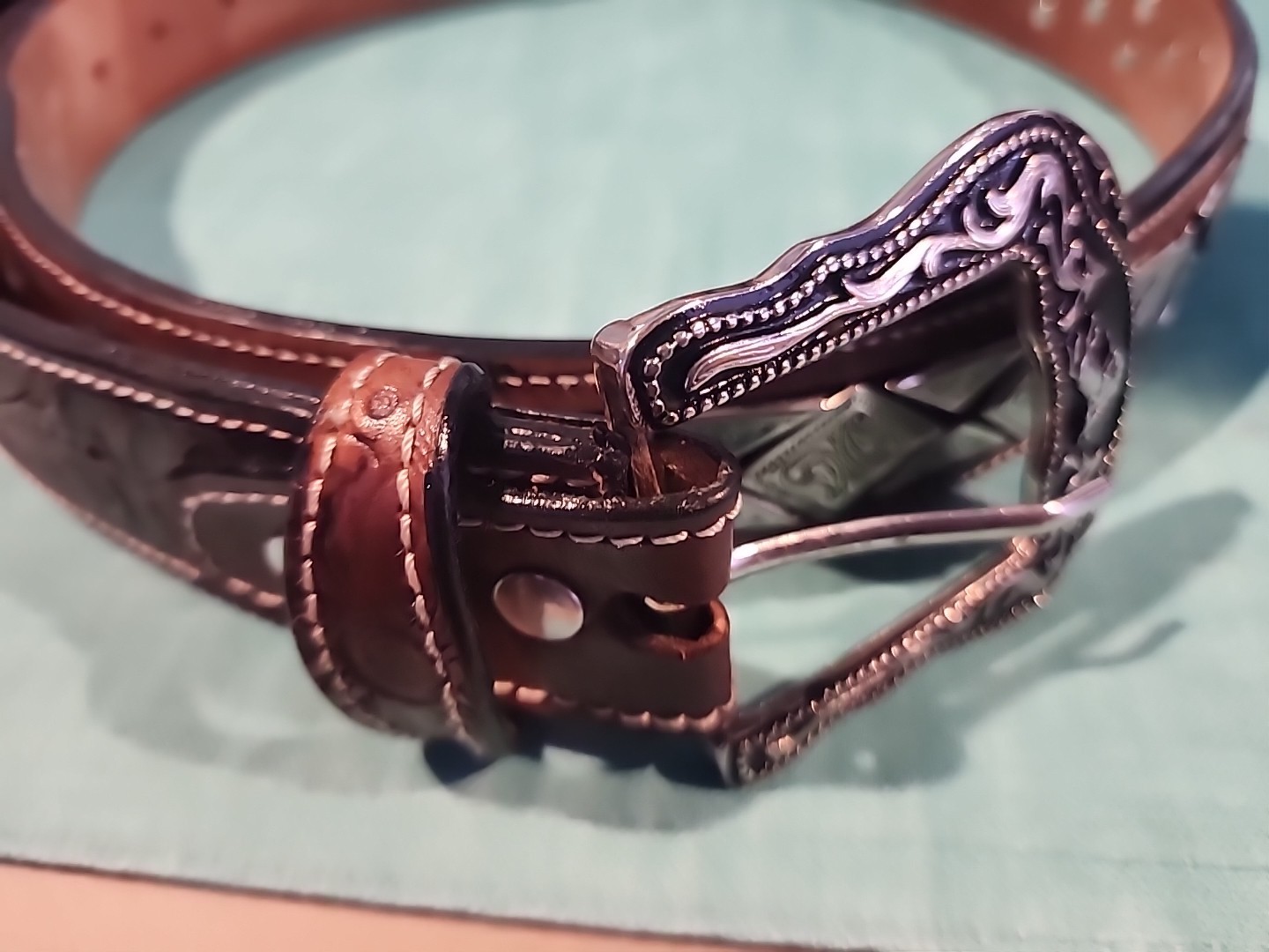 Western belt in basketweave texture featuring floral-engraved buckle in…
