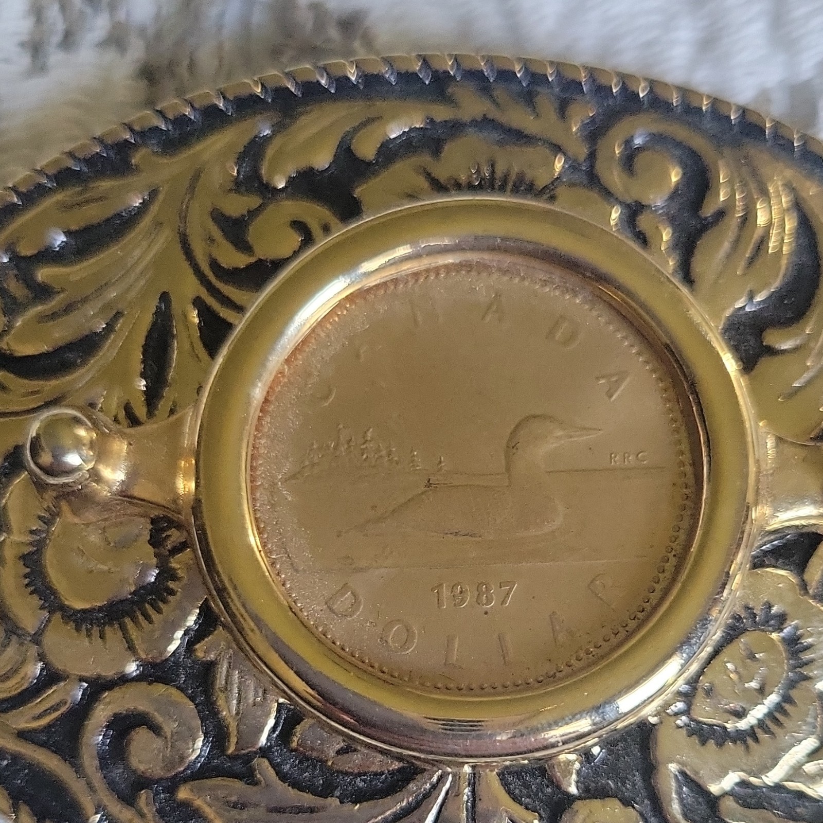 Vntage, gold-toned oval belt buckle features 1987 Canadian One Dollar Coin