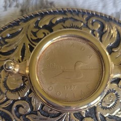 Vntage, gold-toned oval belt buckle features 1987 Canadian One Dollar Coin