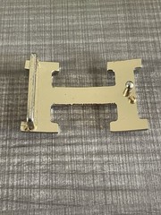 This is a gold-plated Hermès H Quizz belt buckle featuring a black lacquer inlay